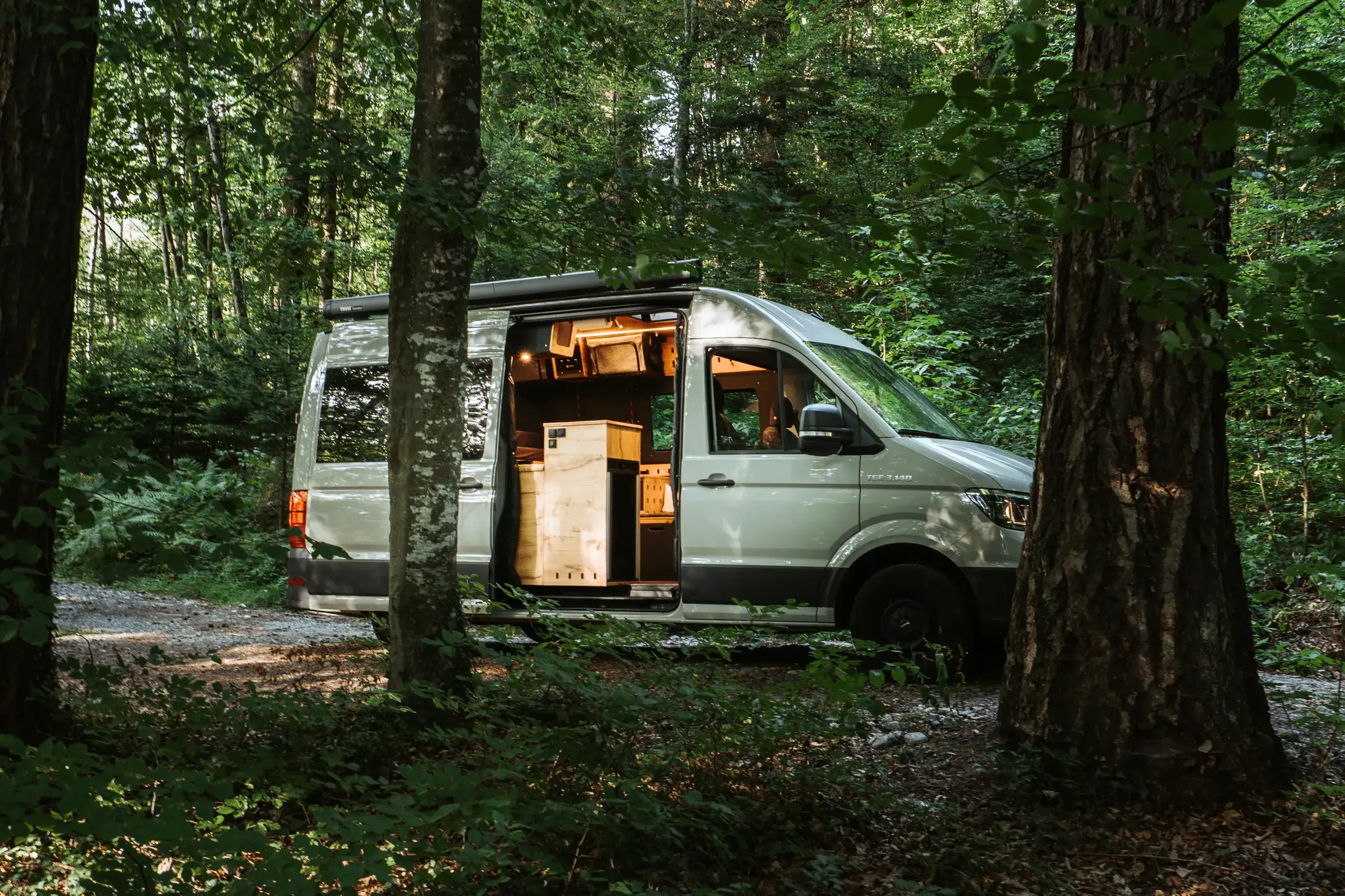 Castello Camper im Wald – Kastenwagen mit geöffneter Schiebetür, Blick auf den beleuchteten Echtholz-Ausbau